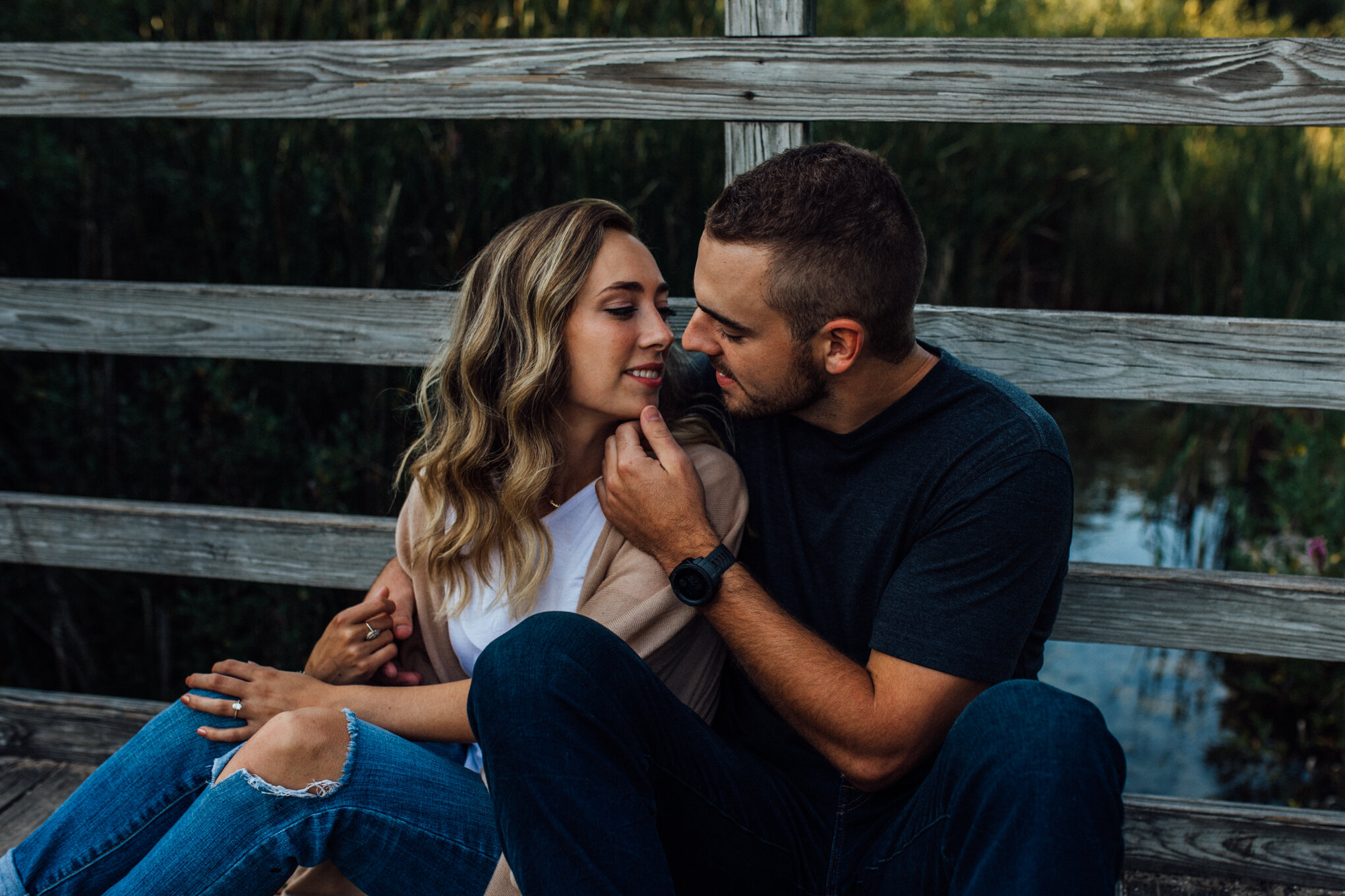  engaged couple sitting on wood bridge leaning into each other 