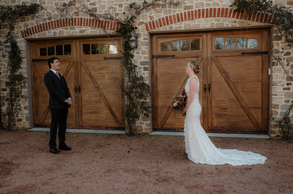 bride and groom seeing each other for the first time on their wedding day, standing in front of two wood carriage doors on a brick building with vines