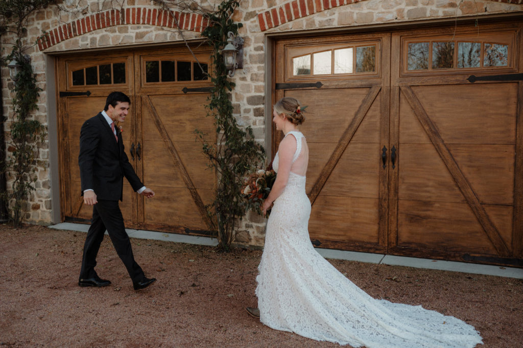 groom walking towards bride as they see each other for the first time on their wedding day, standing in front of two wood carriage doors on a brick building with vines