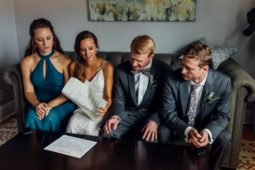 Bride and groom  and witnesses sign marriage certificate on couch after ceremony at Birch