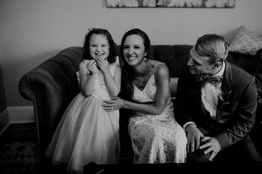 Bride poses with little girl showing her new lost tooth on couch after ceremony at Birch