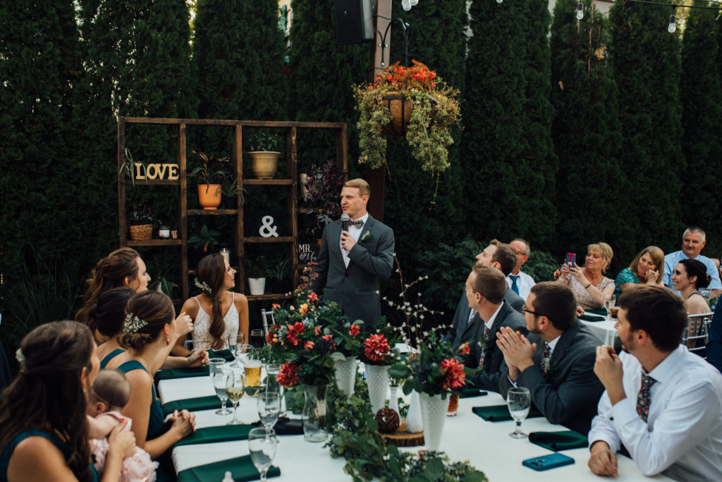 Groom stands and speaks during dinner on patio at Birch, wauwatosa outdoor wedding venue