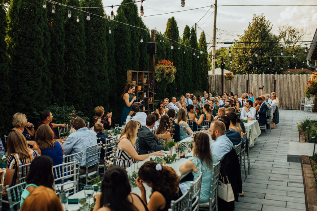 Wide shot of bridesmaid's speech during dinner on outdoor patio at Birch while bride and groom laugh