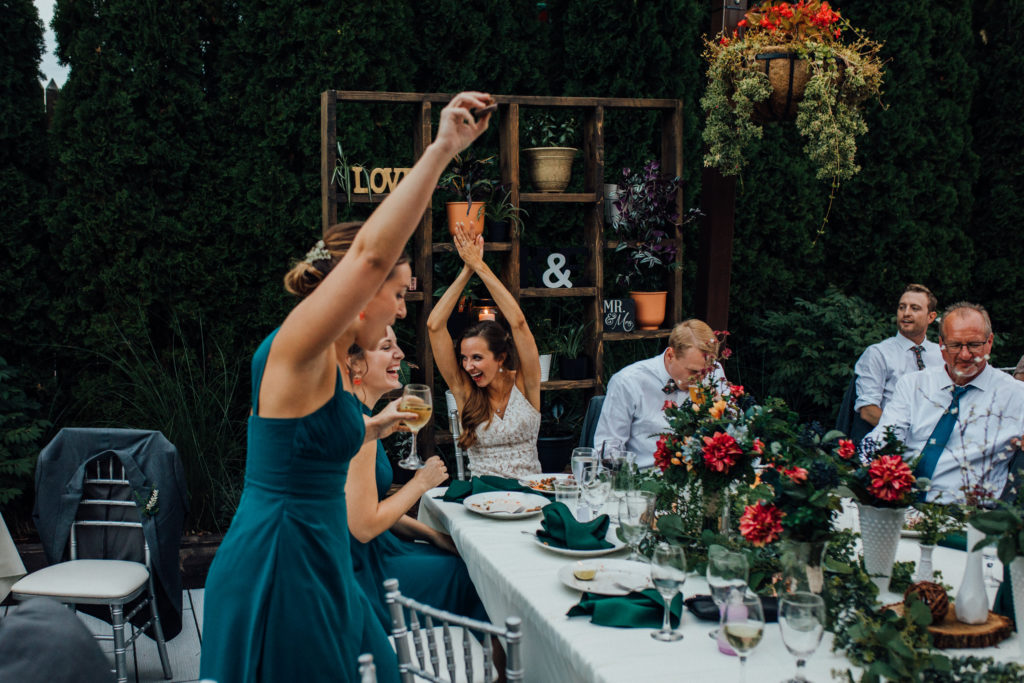 Bride and bridesmaids laughing with hands in the air during dinner on patio at Birch