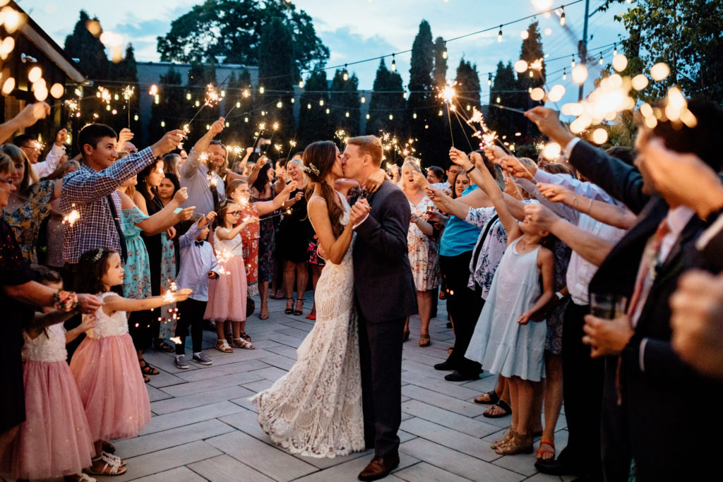 bride and groom embrace  and kiss with sparklers illuminating them on patio of wauwatosa outdoor wedding