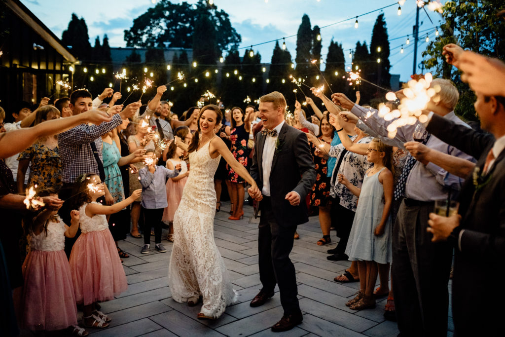 bride and groom dance with golden sparklers illuminating them on patio