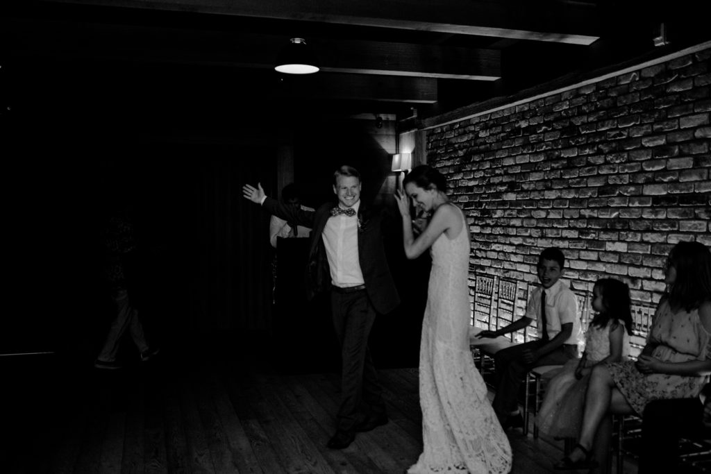 Groom holds out arm while he and bride are welcomed to the dancefloor in black and white