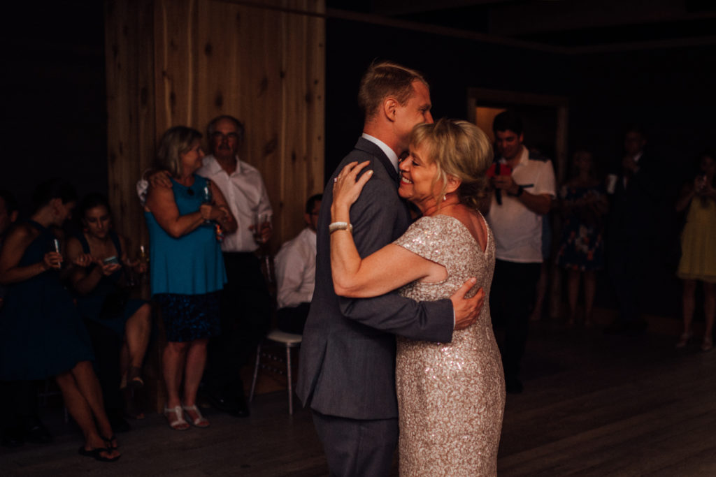 Mother closes her eyes and laughs while dancing with groom laughing during first dance
