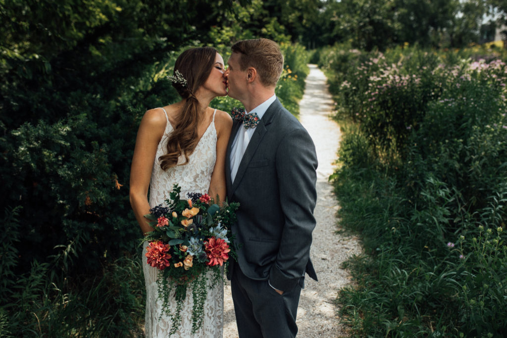 Bride and groom kiss on path among wildflowers