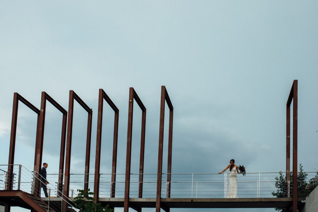 Bride + groom stand on bridge above Lakefront Brewery