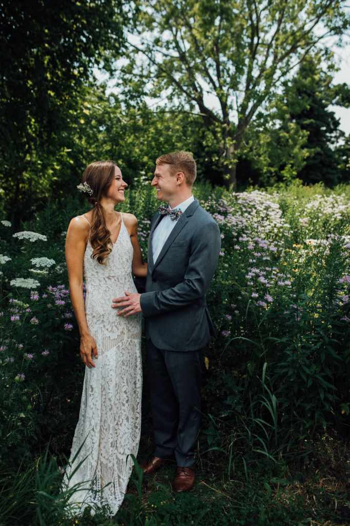 Bride and groom laugh while standing among tall wildflowers