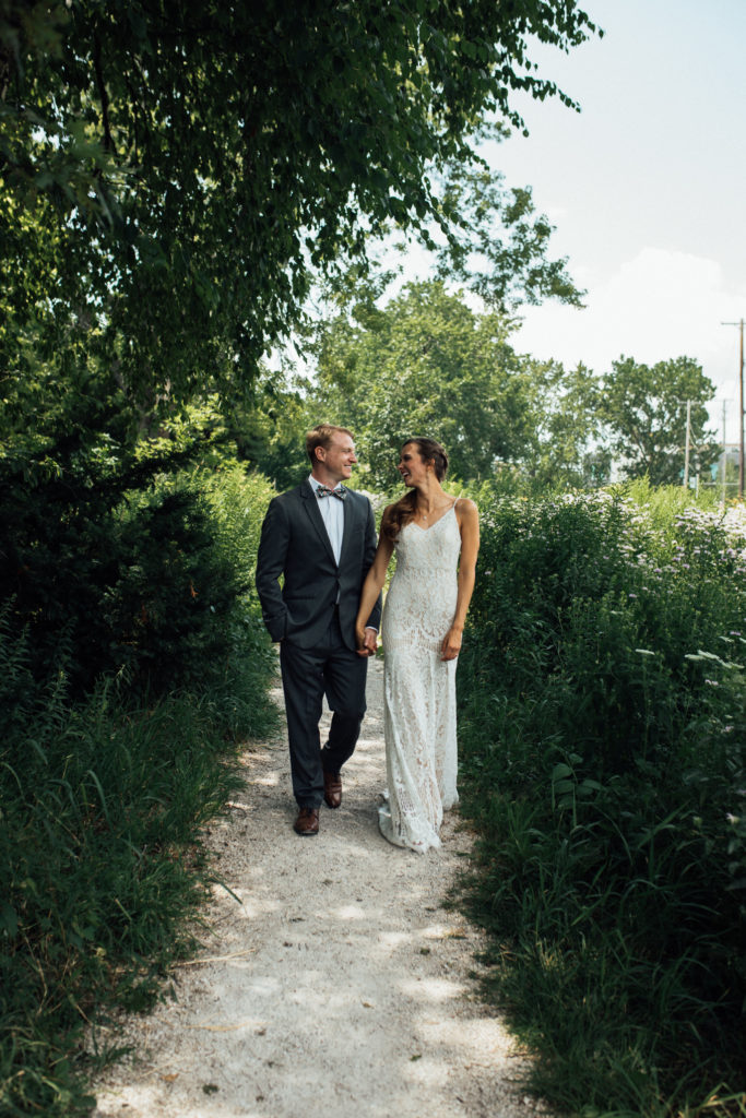 Bride and groom laugh while walking down path with wildflowers