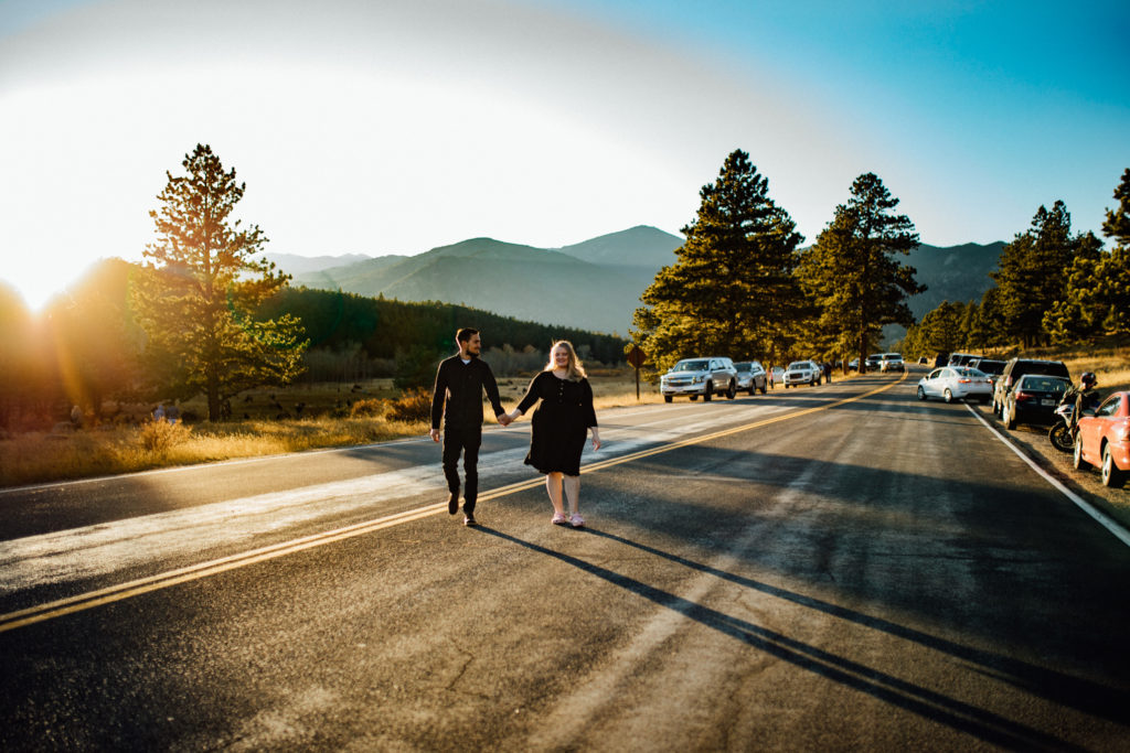 couple holds hands and crosses street during sunset in rocky mountain national park