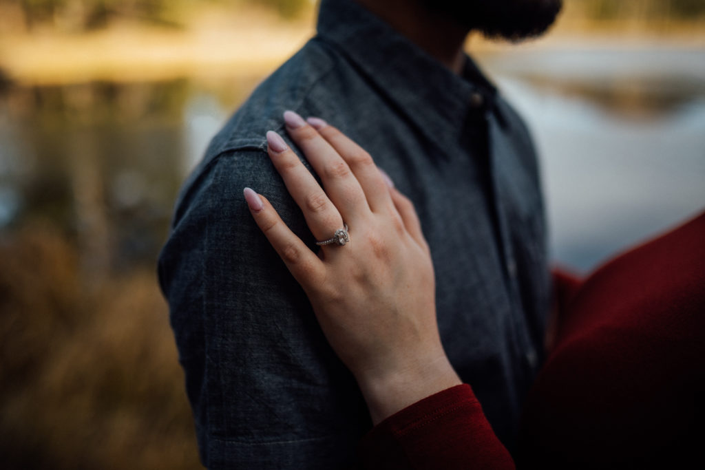 Girl with right hand on man's shoulder with engagement ring