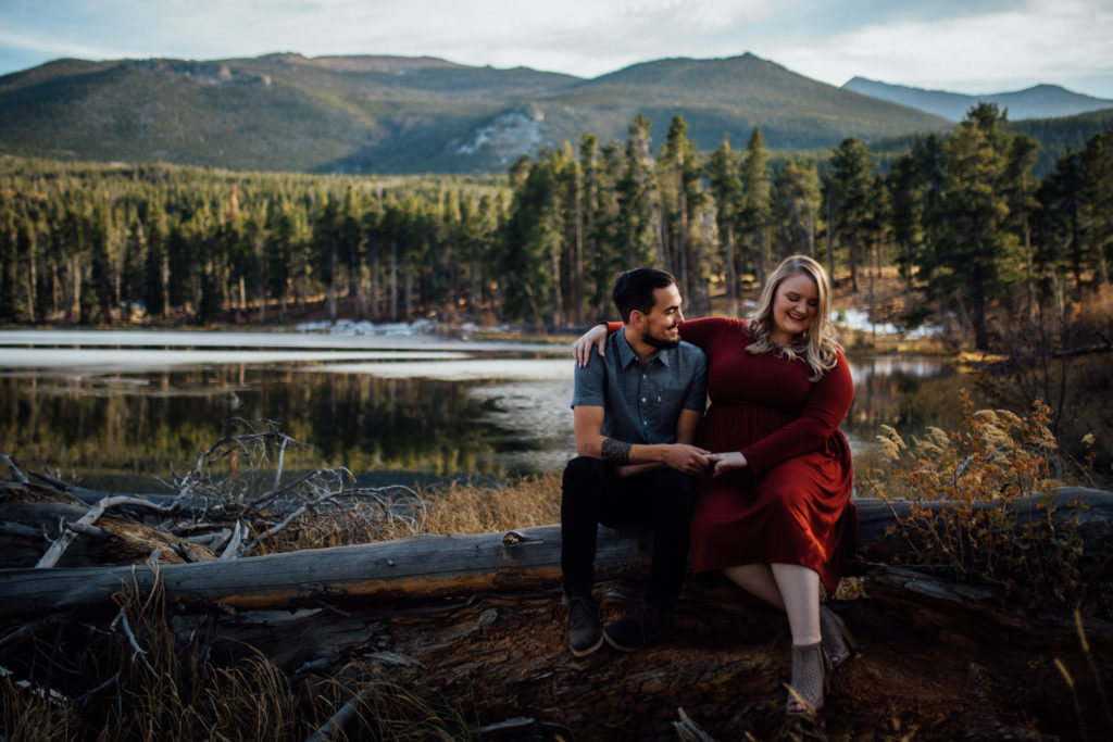 Man and woman sit on log in front of Sprague Lake with mountains