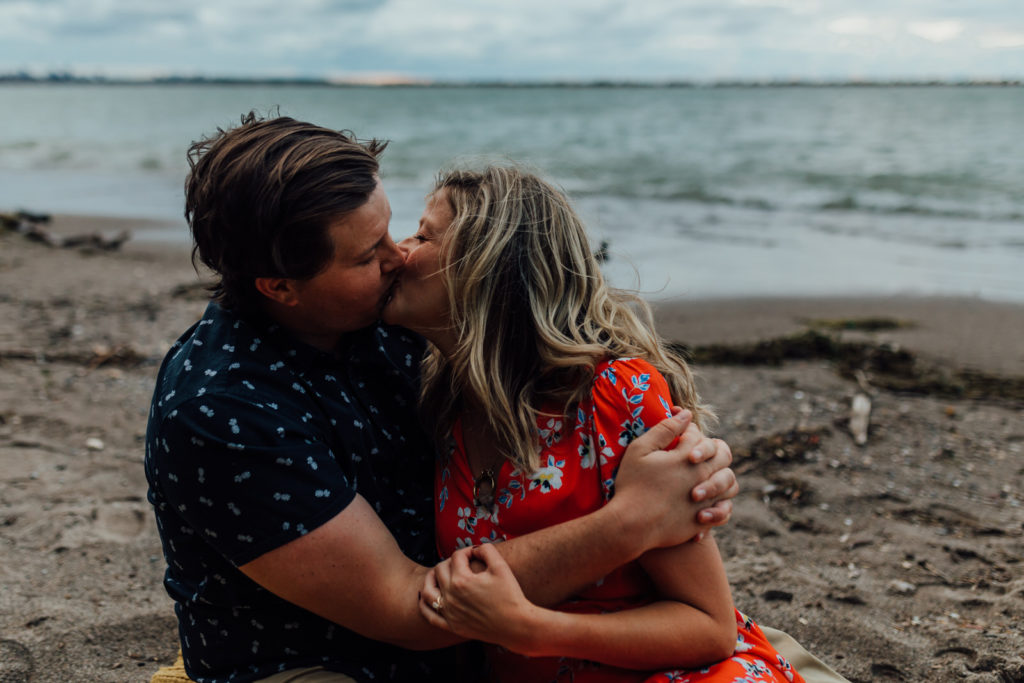 Engaged man and woman sitting on beach kissing and embracing