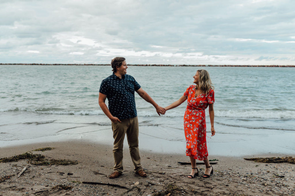 engaged man and woman hold hands and laugh on the beach