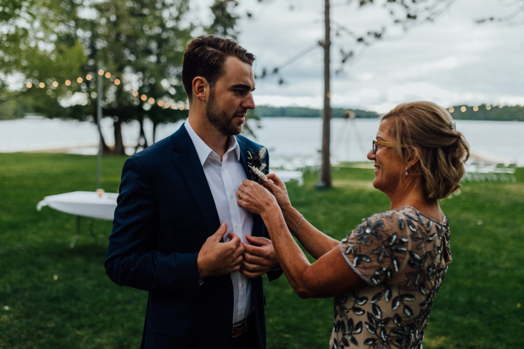 grooms mother pins on boutonniere by the lake