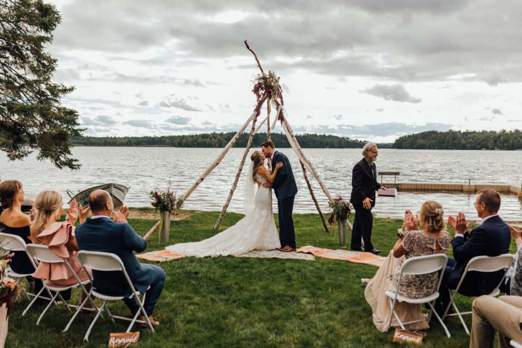 bride and groom share first kiss under birch tipi during intimate boho wedding ceremony in wisconsin