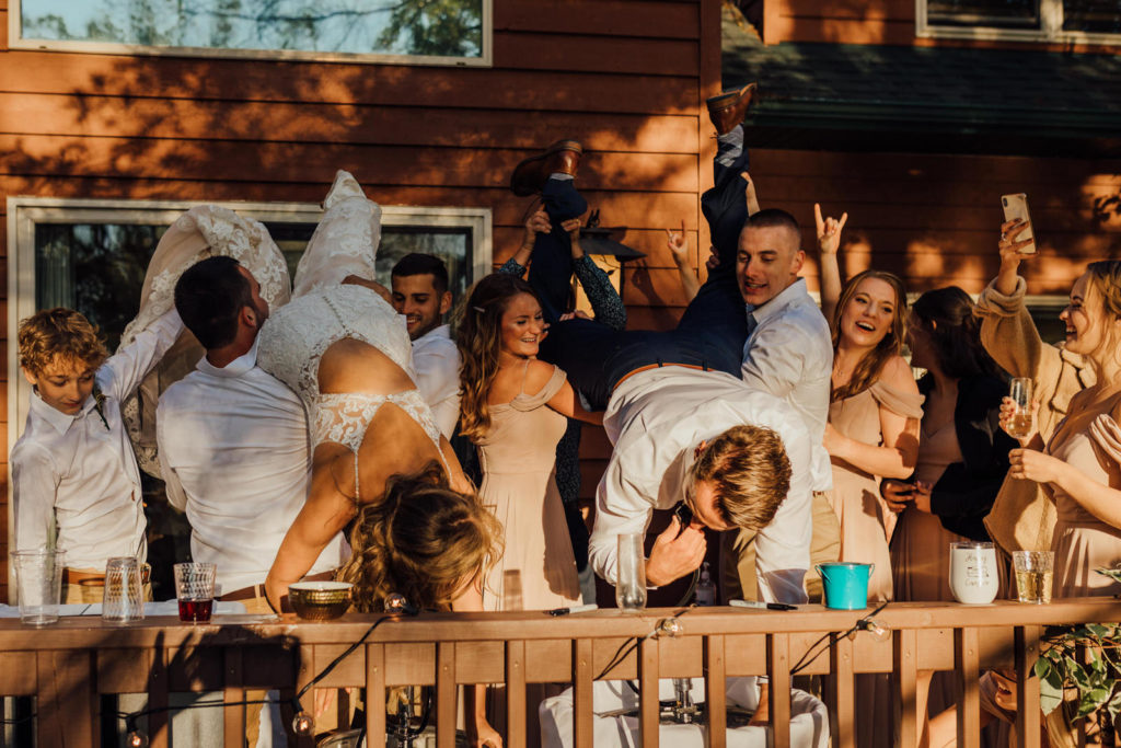 friends hold bride and groom up for double keg stand on deck